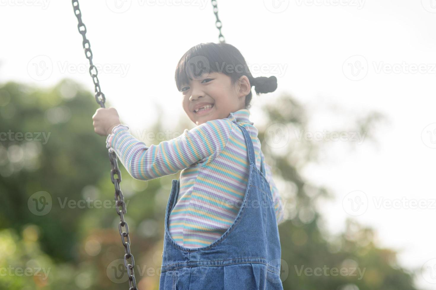 heureuse petite fille asiatique jouant à la balançoire en plein air dans le parc photo