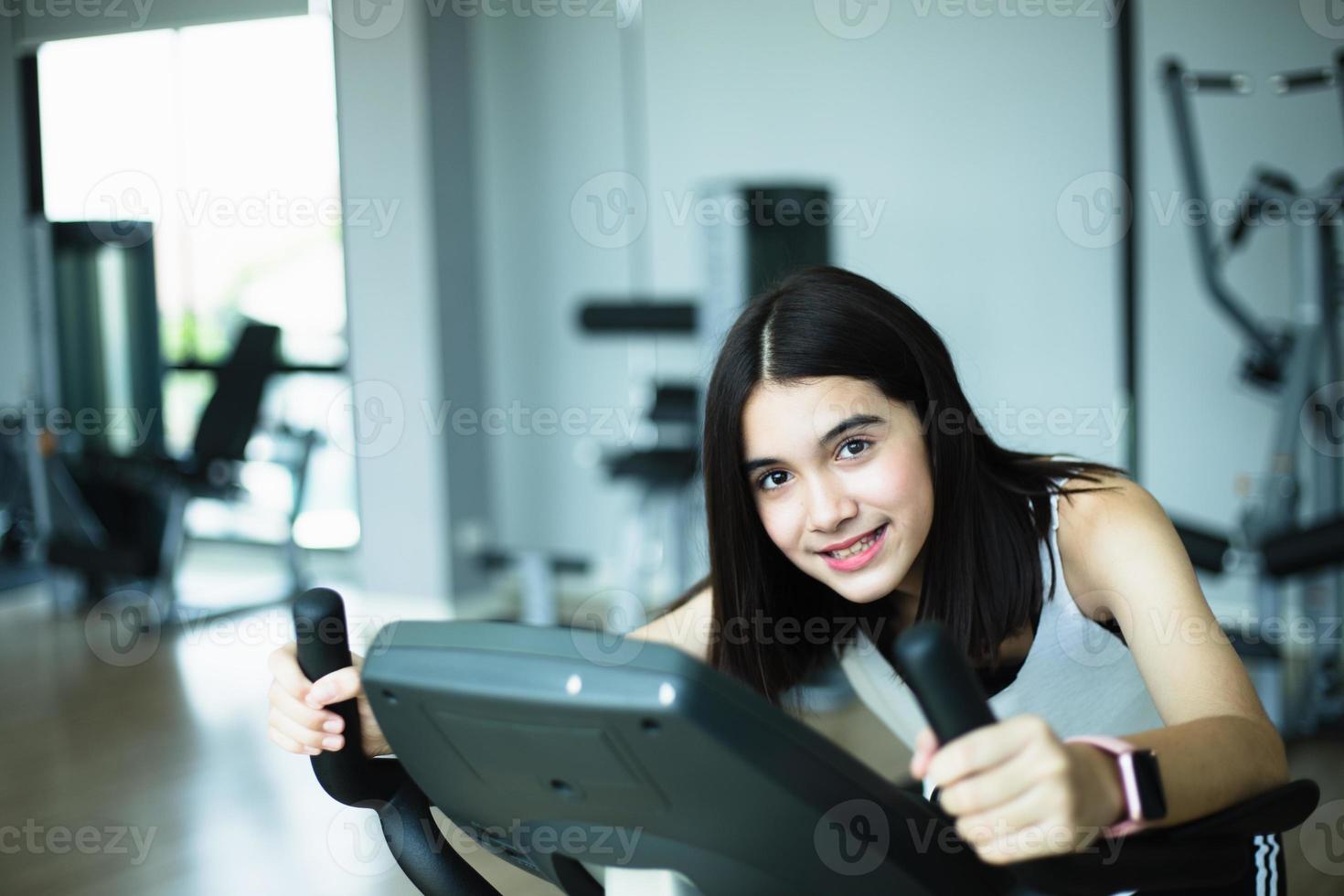 fit jeune fille à l'aide d'un vélo d'exercice à la salle de gym. femme de remise en forme à l'aide d'un vélo pneumatique au gymnase. photo