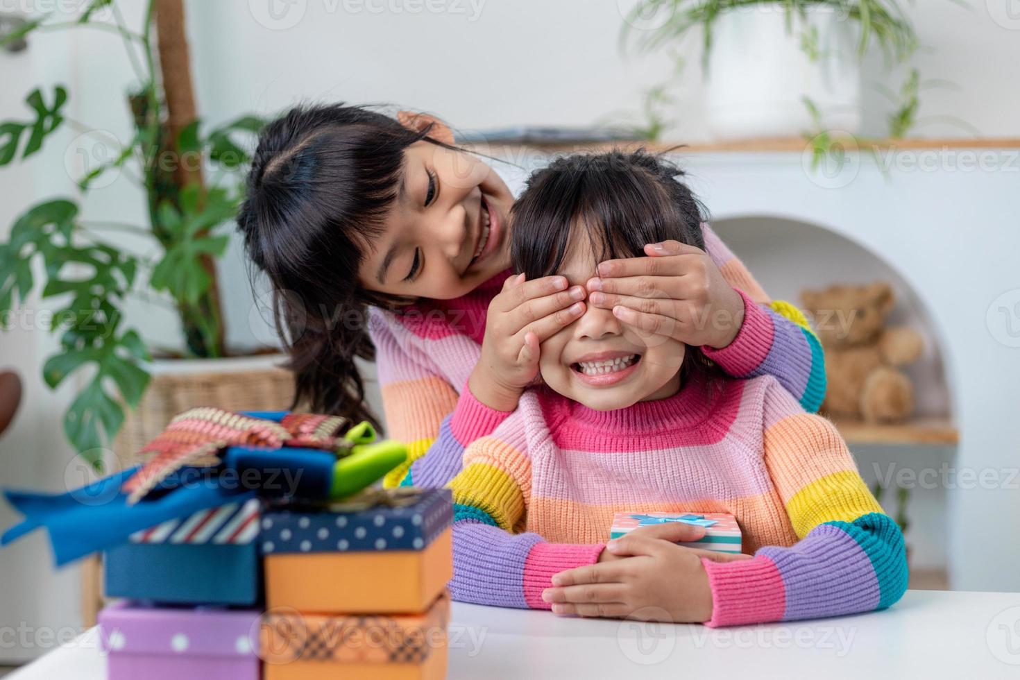 petite fille faisant un cadeau à une petite fille heureuse tenant une boîte-cadeau, fermant les yeux d'un joli sourire excité par la surprise d'anniversaire de sa sœur photo