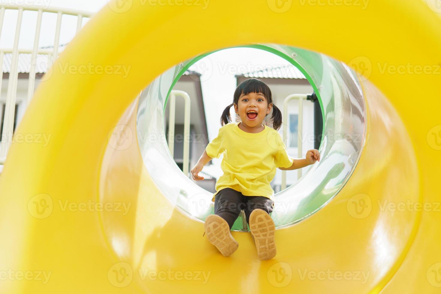 enfant jouant sur une aire de jeux extérieure. les enfants jouent dans la cour de l'école ou de la maternelle. enfant actif sur un toboggan et une balançoire colorés. activité estivale saine pour les enfants. photo