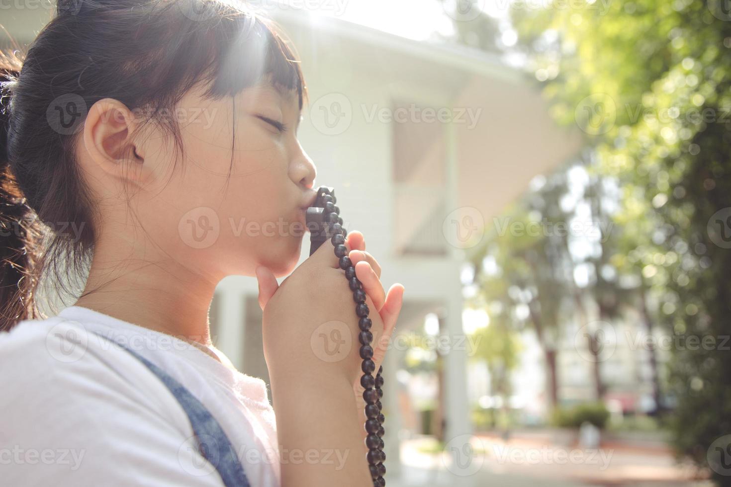 petite fille asiatique priant en tenant la croix, concept chrétien. photo