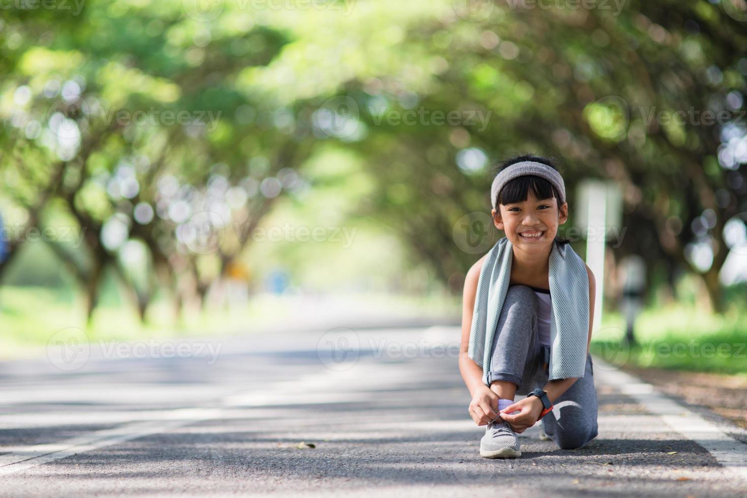 enfant attachant des chaussures de course. heureuse drôle petite fille asiatique fitness femme courant le matin. jeune enfant athlétique courant dans la nature. mode de vie sain photo