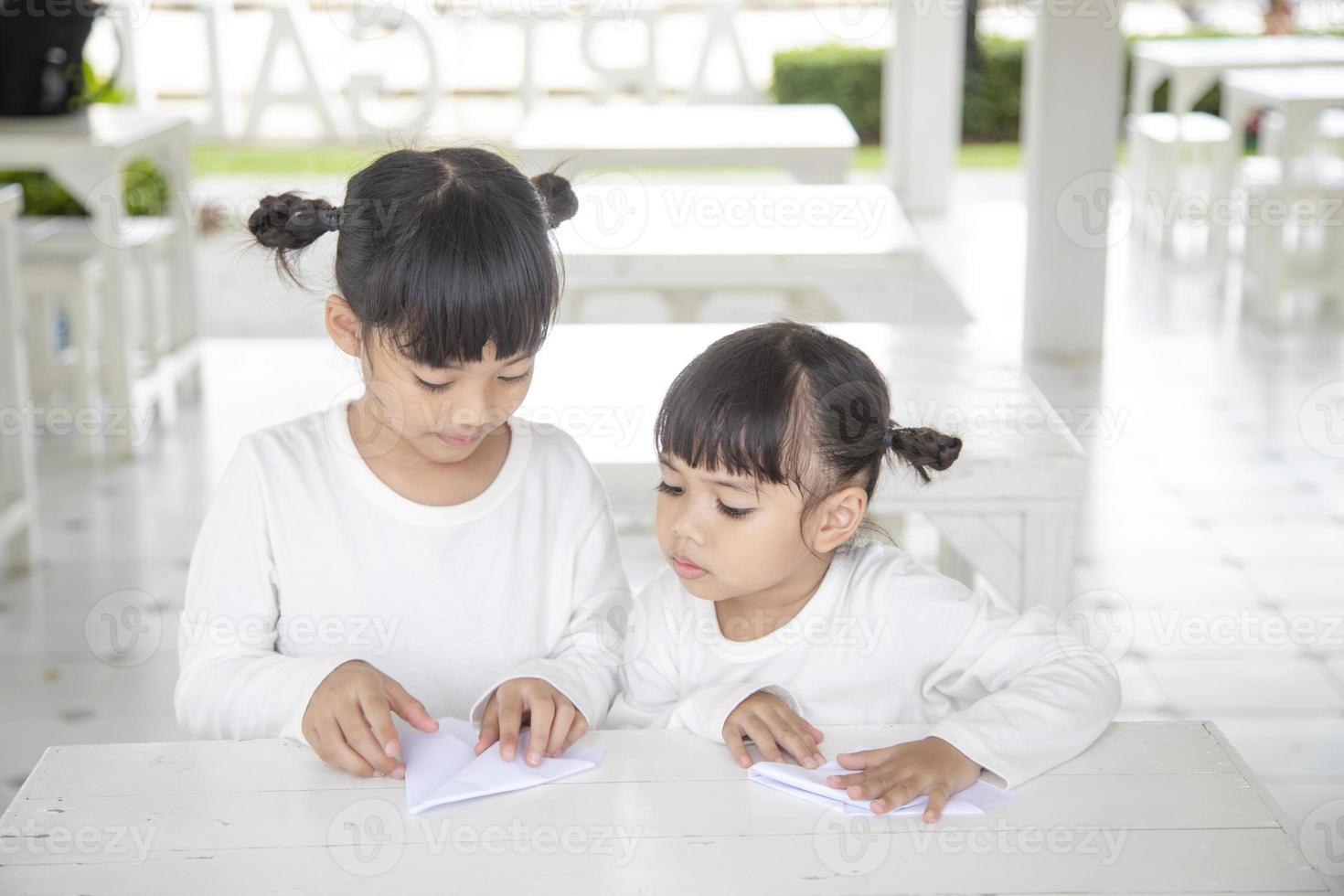 les frères et sœurs asiatiques assis sur la table créent un avion en papier. photo