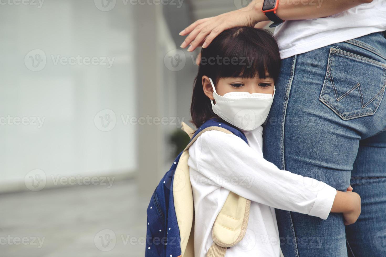 la mère accompagne l'enfant à l'école. maman soutient et motive l'élève. la petite fille portant un masque facial ne veut pas quitter sa mère. craint l'école primaire. photo