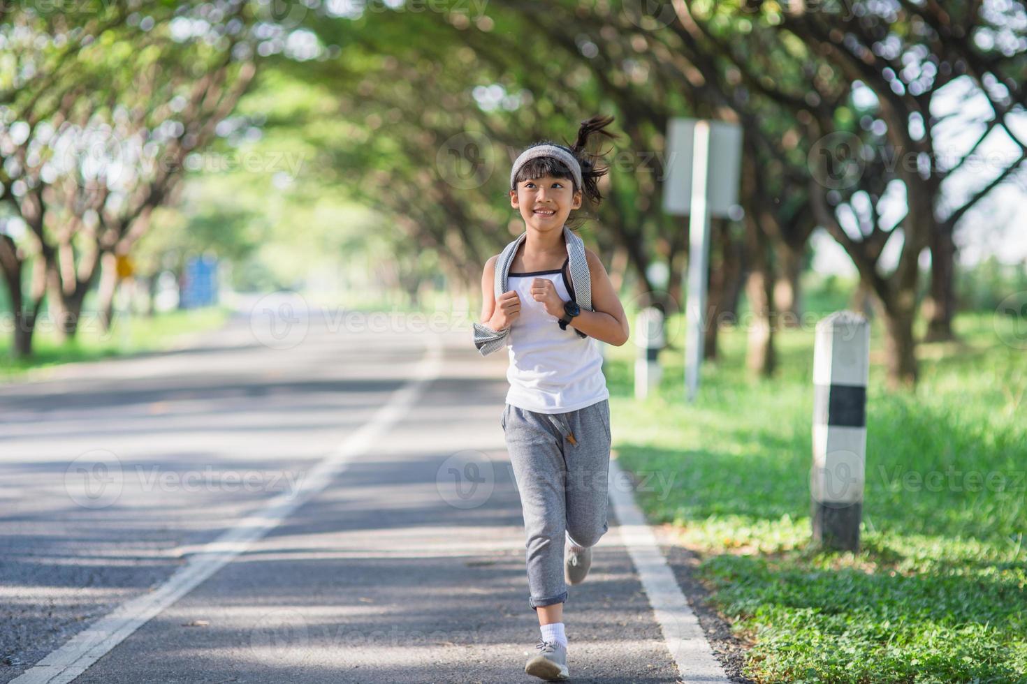 fille enfant heureuse qui court dans le parc en été dans la nature. lumière du soleil chaude. le petit asiatique court dans un parc. sports de plein air et fitness, apprentissage de l'exercice et de la compétition pour le développement des enfants. photo