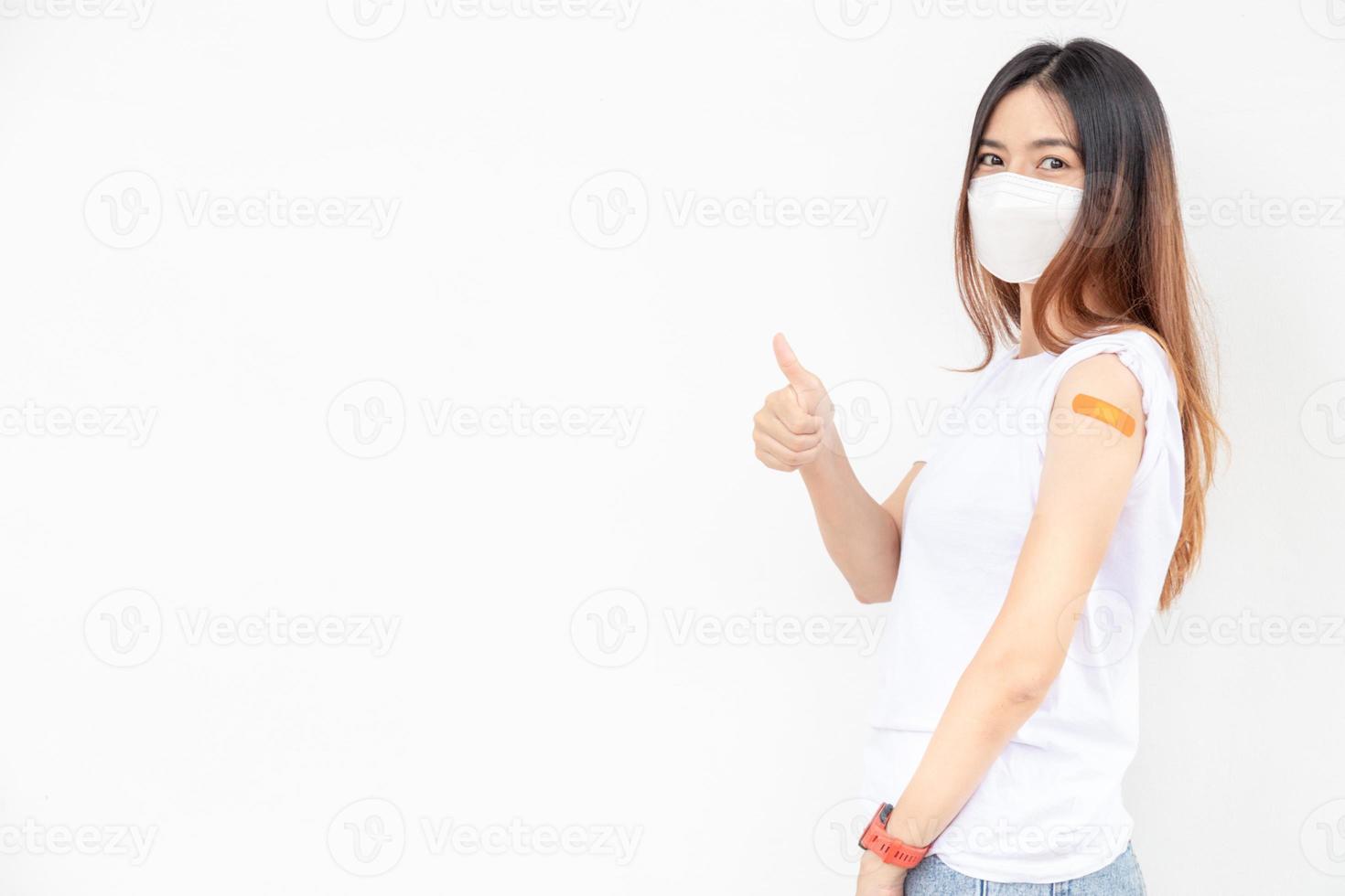 les femmes asiatiques montrent un bandage sur le bras. une femme asiatique heureuse se sent bien après avoir reçu le vaccin sur fond blanc.pouce vers le haut. photo