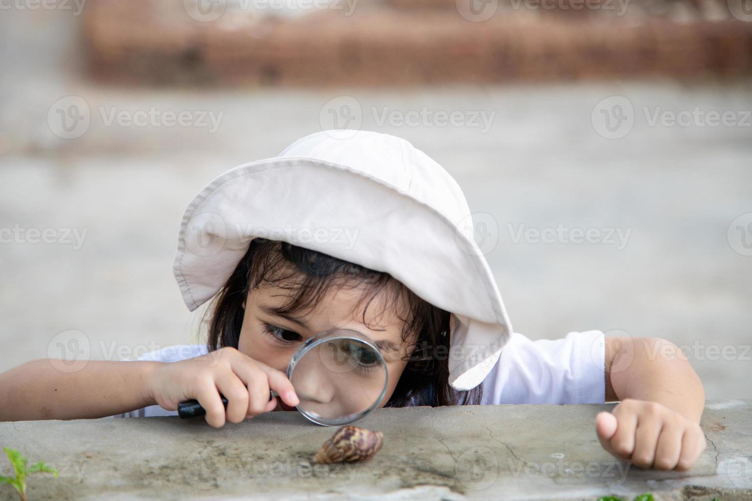 bonne petite fille explorant la nature avec une loupe et un escargot. il s'amuse dans le jardin. le concept de l'enfant est prêt à aller à l'école. photo