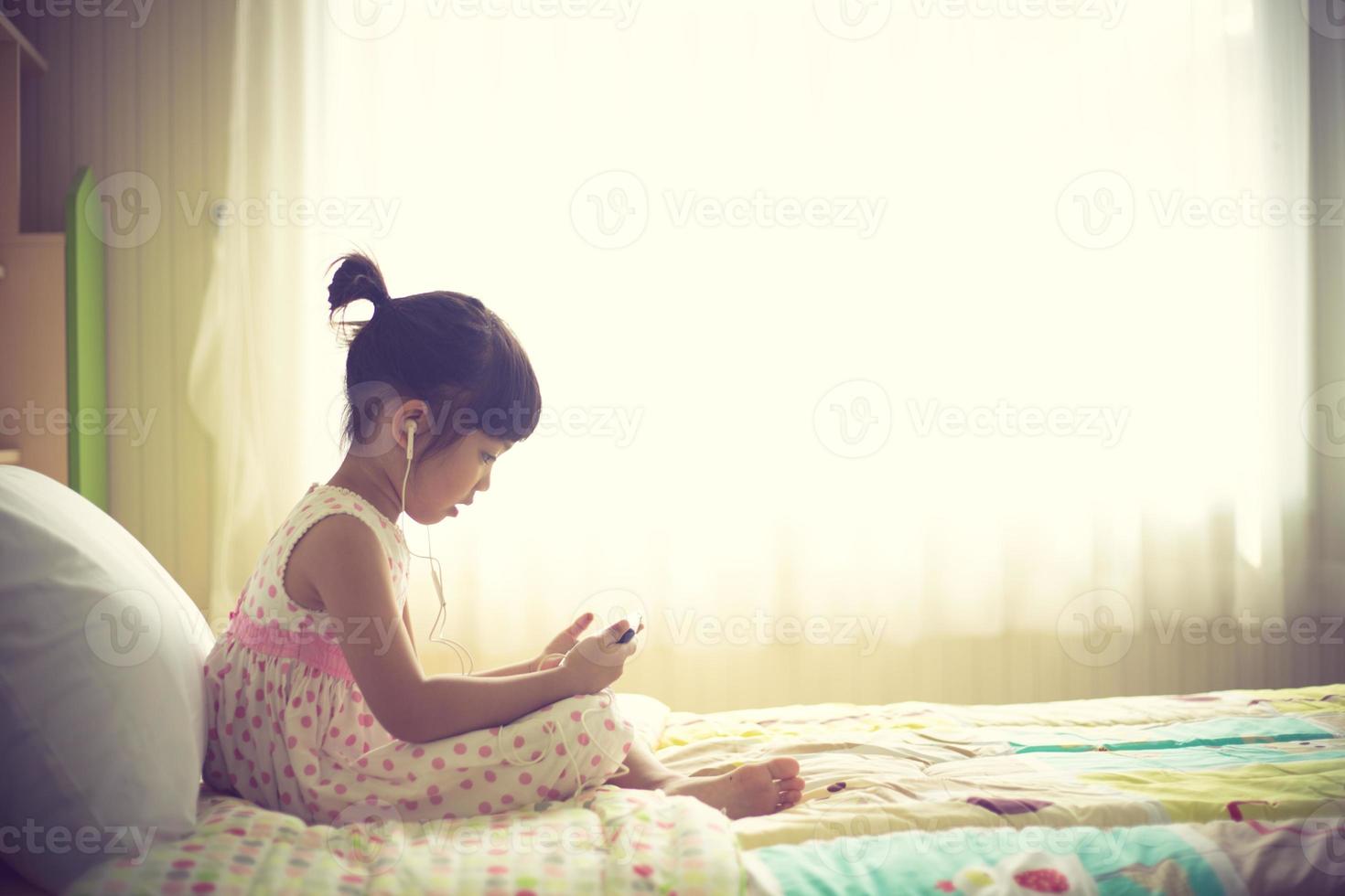 enfants asiatiques utilisant un casque pour écouter de la musique par smartphone sur le lit dans sa chambre décorée photo