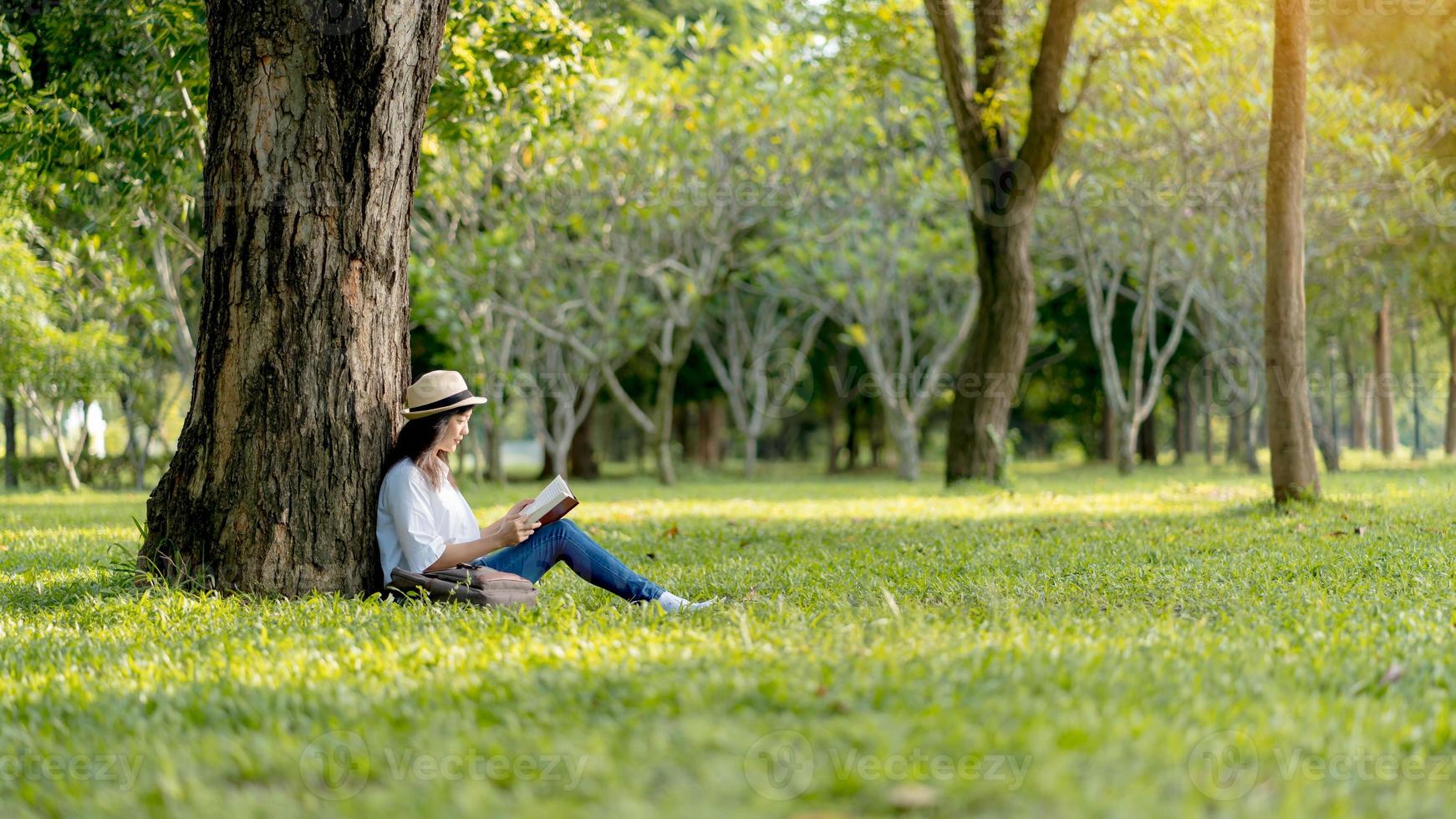 une femme asiatique se détend en s'asseyant joyeusement en lisant un livre dans le parc. photo