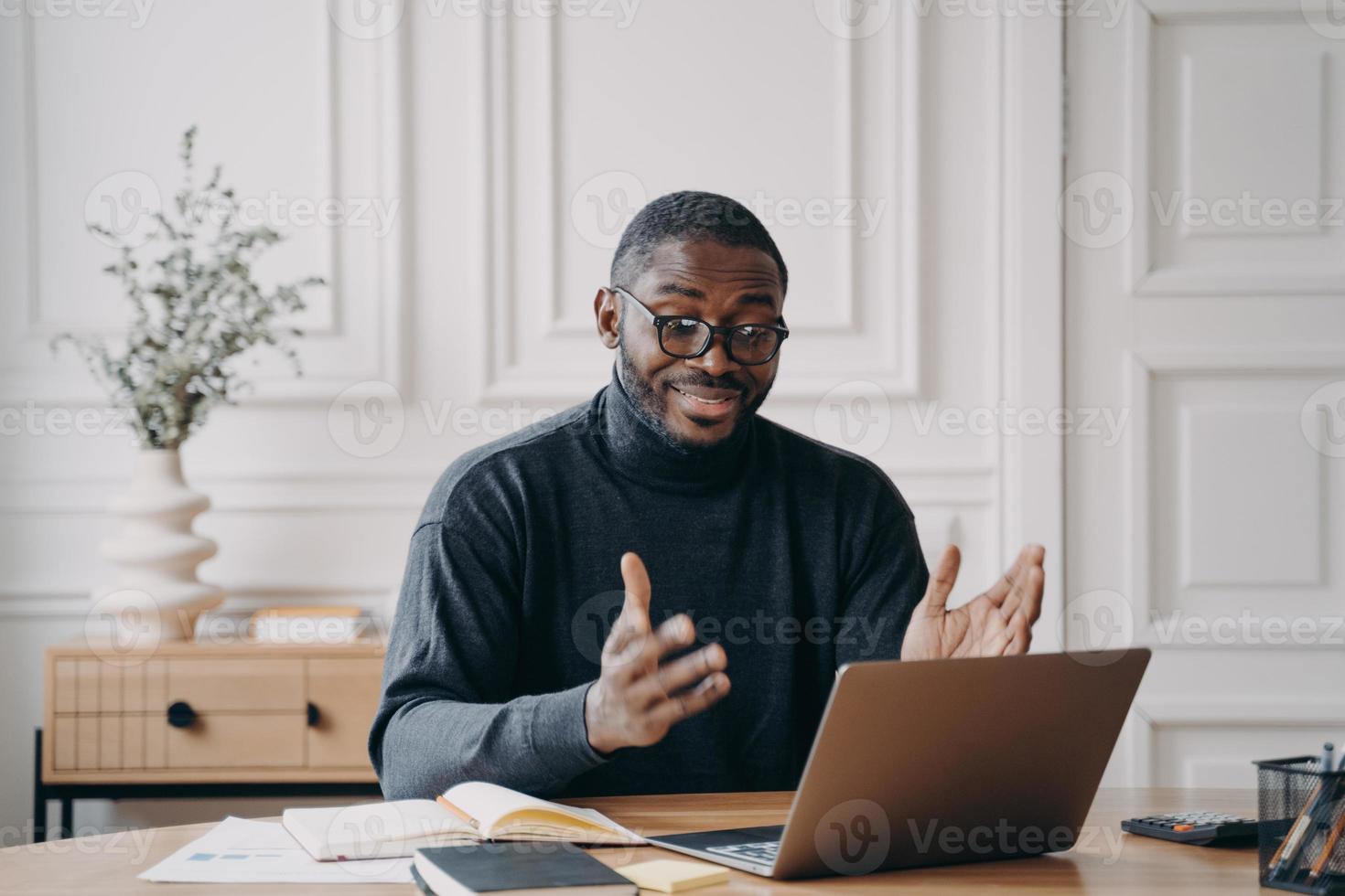 jeune tuteur afro-américain positif parlant avec des étudiants pendant la leçon en ligne sur ordinateur portable photo