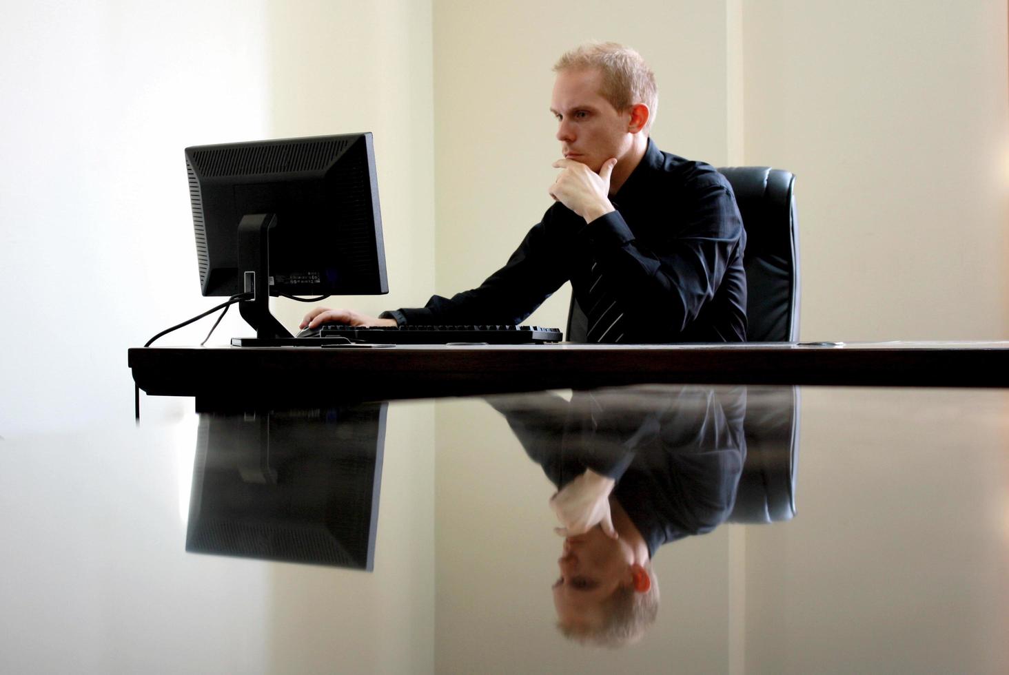 homme caucasien blanc assis à l'ordinateur derrière un bureau en verre photo