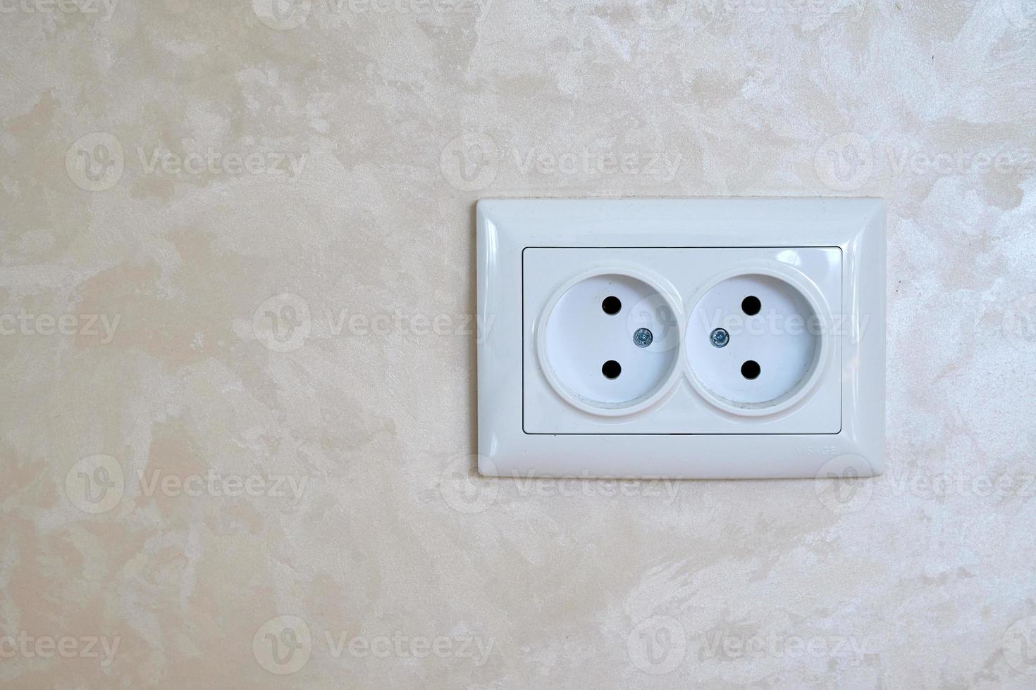 prise électrique blanche en deux parties sur un mur beige. photo