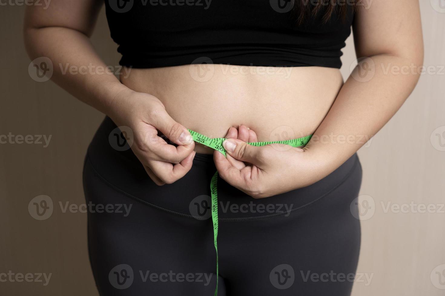 main de grosse femme tenant la graisse du ventre excessive avec ruban à mesurer. grosse femme, gros ventre, potelé. concept de contrôle du poids sain photo