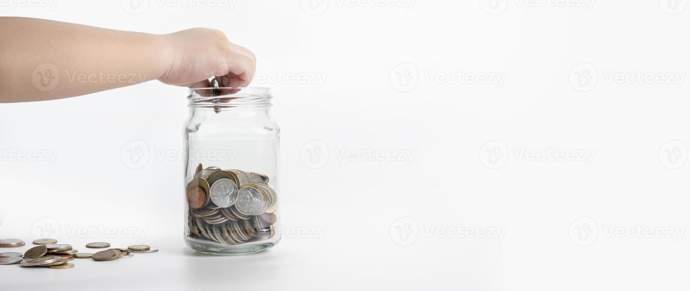 la main de l'enfant met une pièce de monnaie dans un bocal en verre isolé sur fond blanc. concept d'économie d'argent, investissement financier des entreprises, pièce de monnaie dans une bouteille en verre photo