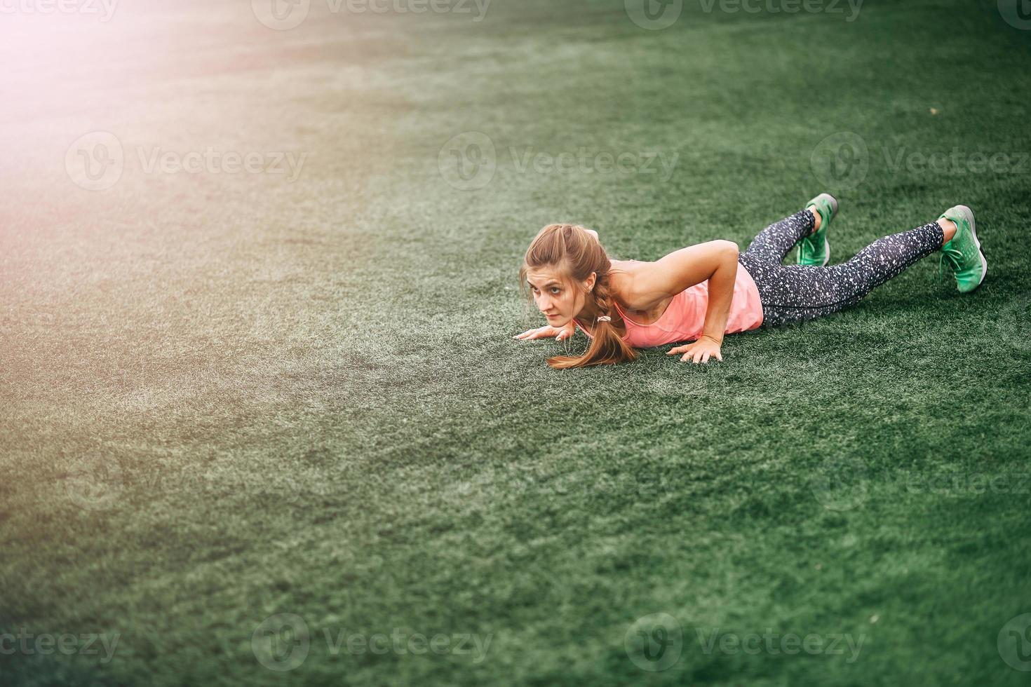 femme en forme dans des vêtements de sport lumineux pour faire des burpees sur l'herbe verte photo