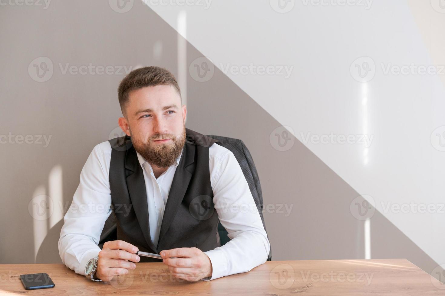 homme d'affaires décontracté barbu, assis à table avec un stylo à la main, pensant photo