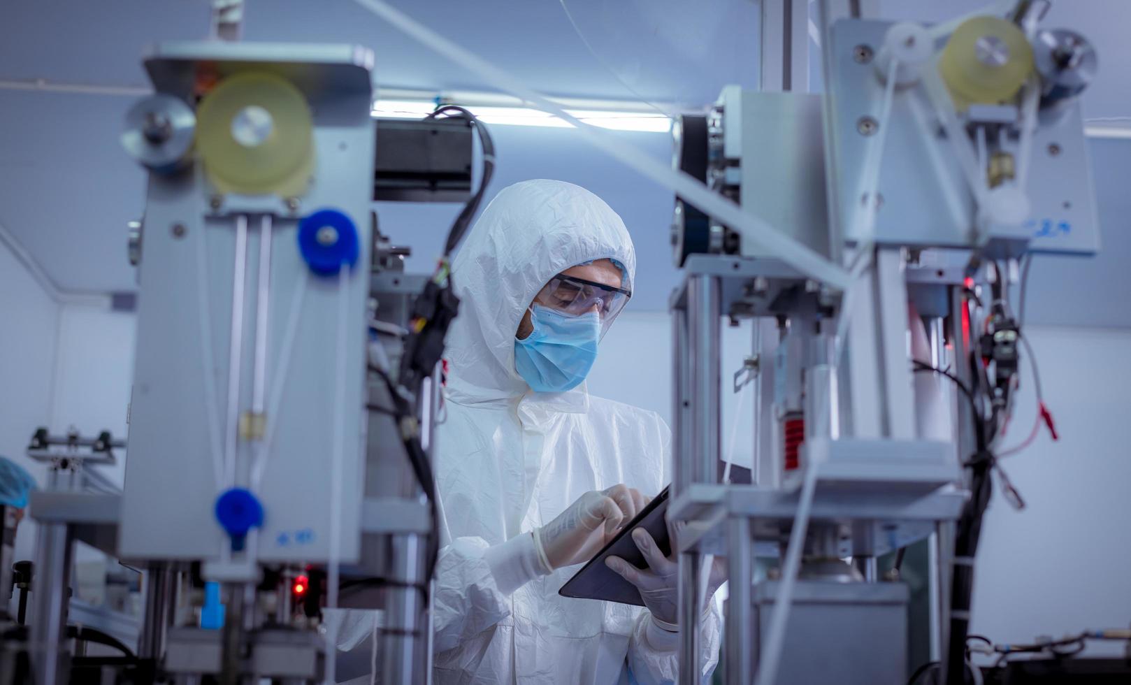 travailleur technicien portant une suite de protection, les gants sont inspectés avec le processus de fabrication du masque facial pour vérifier la sécurité et contre le virus. photo