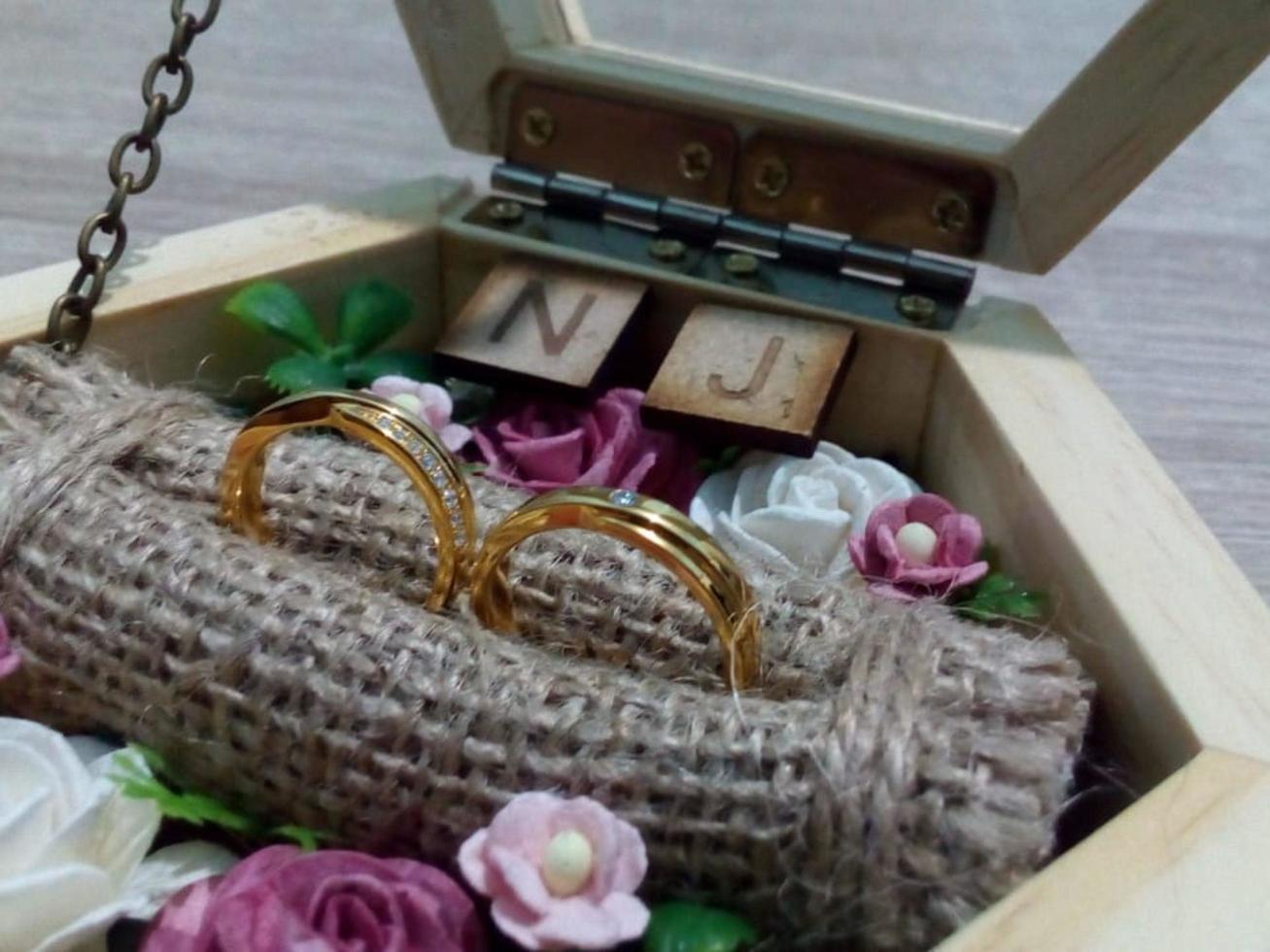 une paire d'alliances et de bagues de fiançailles en or jaune placées sur une boîte à bagues en bois photo