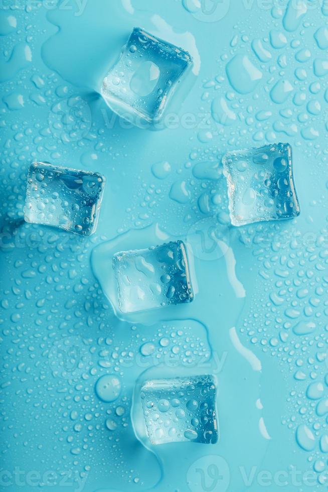 cubes de glace avec des gouttes d'eau éparpillées sur un fond bleu, vue de dessus. photo