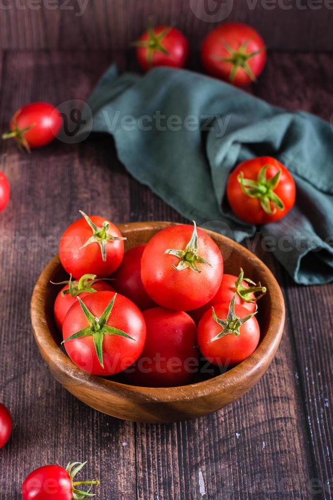 tomates entières crues mûres dans un bol sur une table en bois. récolter les produits locaux. vue verticale photo