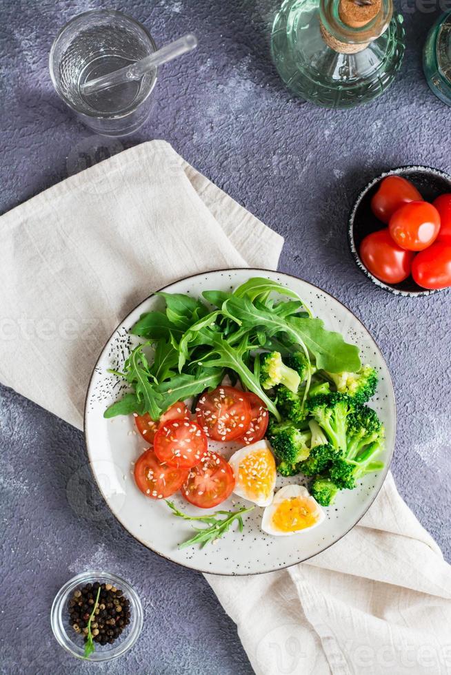 une assiette avec du brocoli, de la tomate, de la roquette, de l'œuf à la coque et des graines de sésame sur une assiette. haut et vertical photo