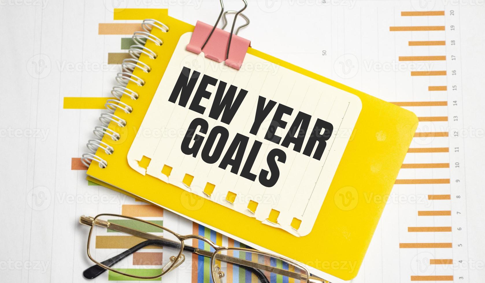 mots d'objectifs du nouvel an sur un autocollant bleu et un cahier jaune avec des graphiques et des lunettes photo