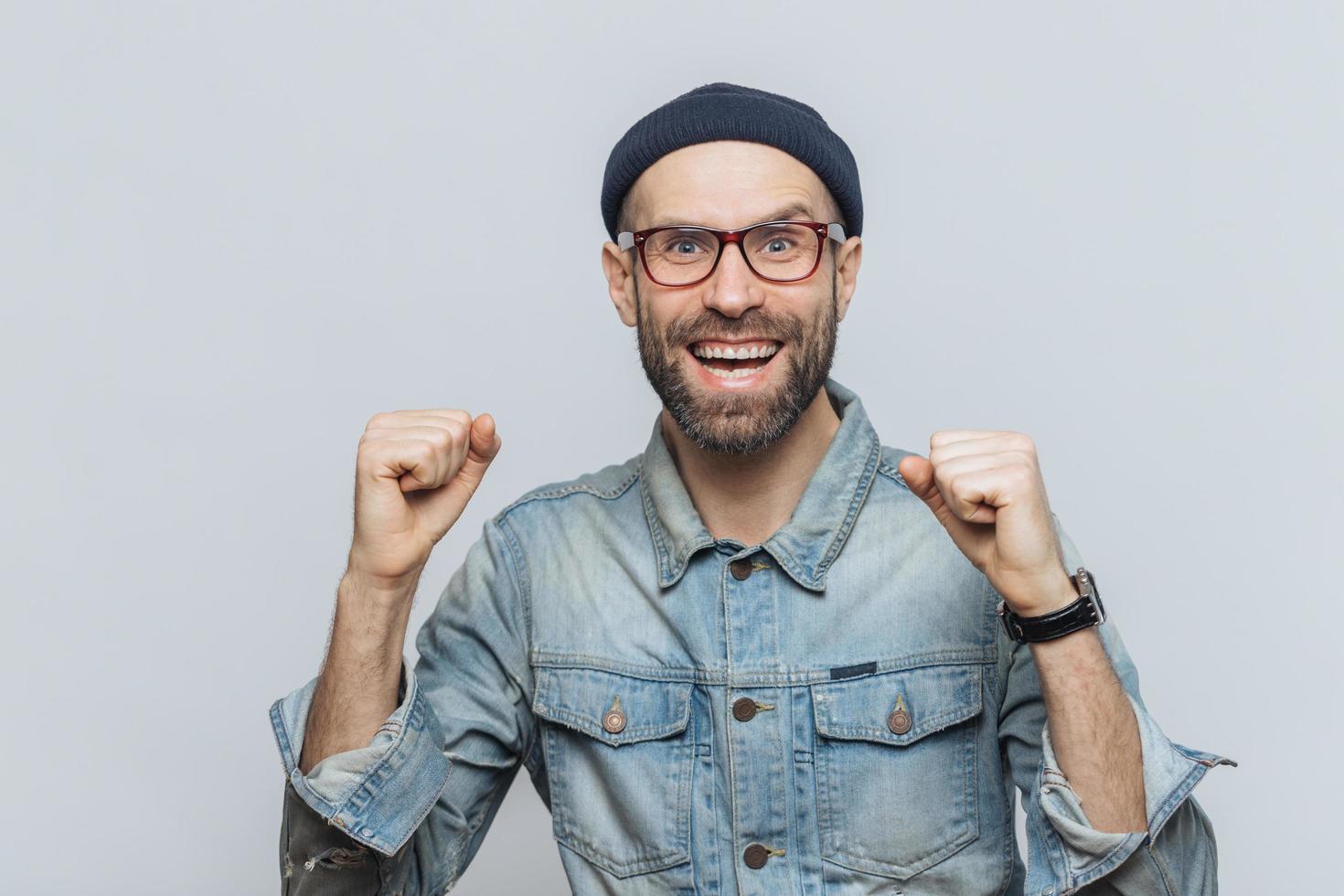 un homme ravi se réjouit de son succès, serre les poings, regarde joyeusement la caméra, isolé sur fond gris. un hipster barbu lève la main avec triomphe. homme d'âge moyen se sent comme un champion photo