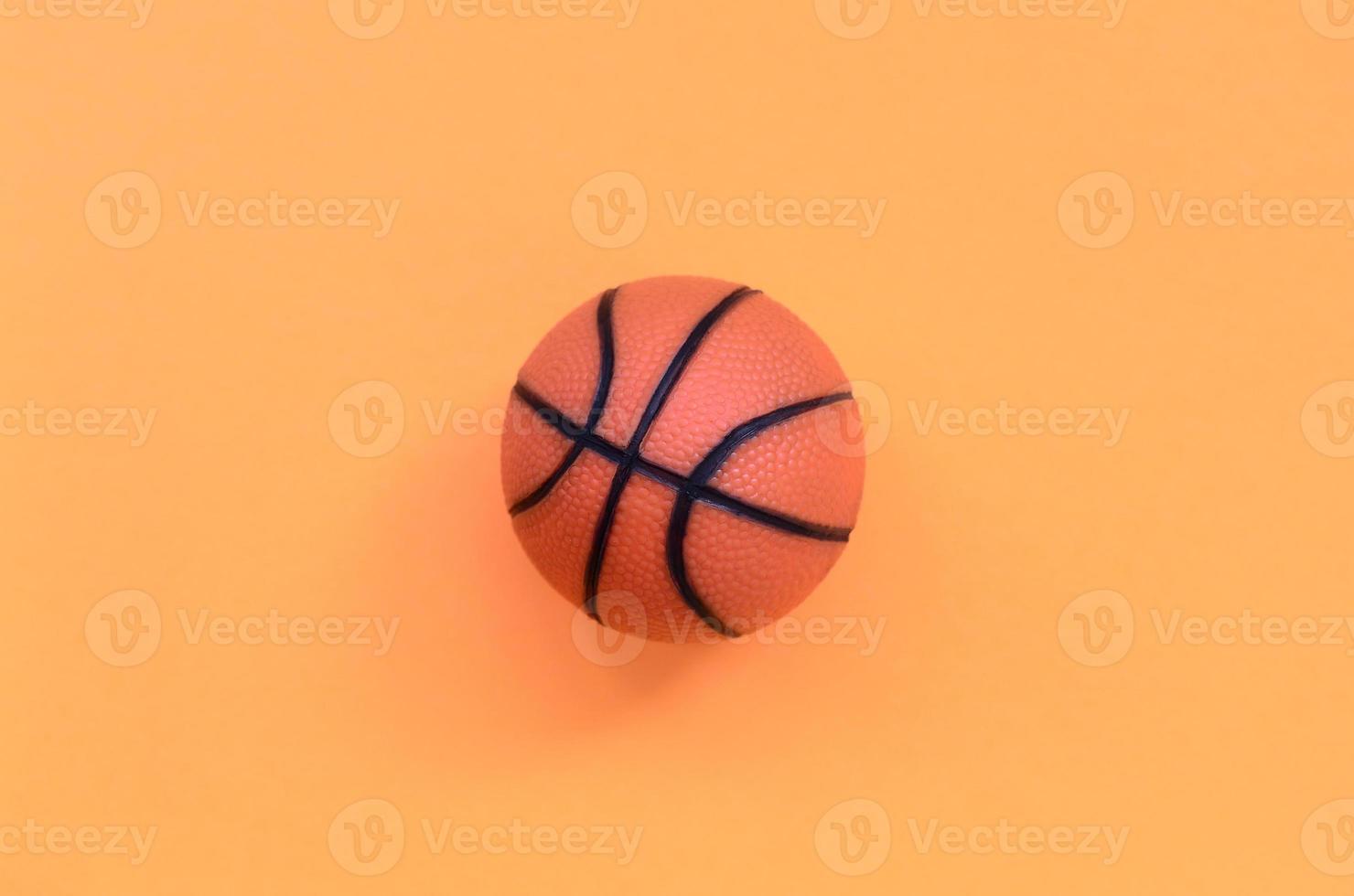 petite balle orange pour le jeu de sport de basket-ball se trouve sur fond de texture de papier de couleur orange pastel mode dans un concept minimal photo