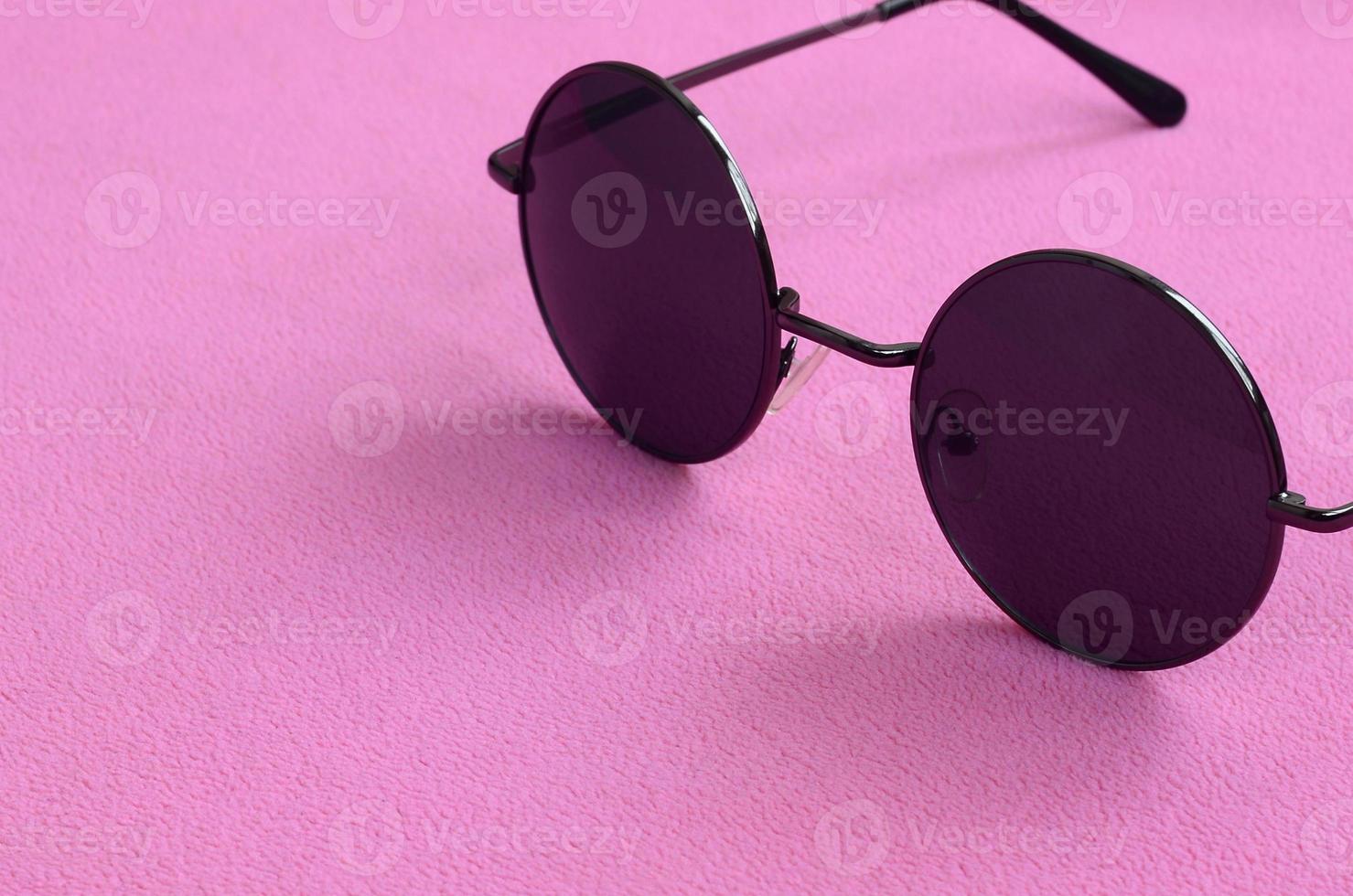 des lunettes de soleil noires élégantes avec des lunettes rondes reposent sur une couverture en tissu polaire rose clair doux et moelleux. image de fond à la mode aux couleurs féminines photo