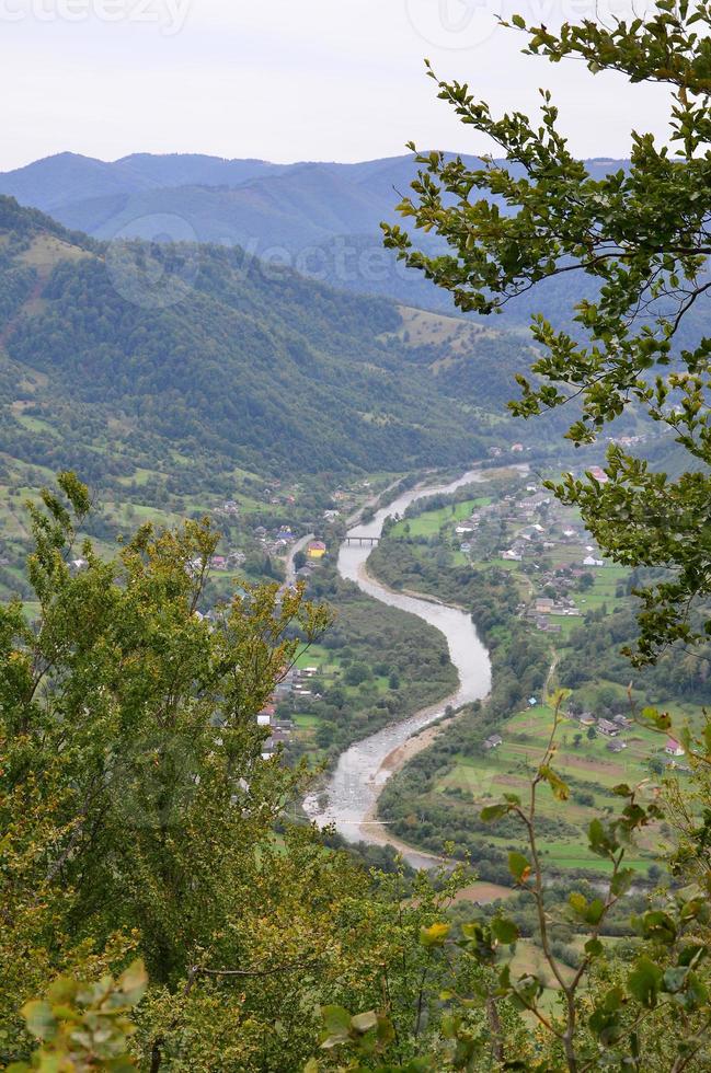 une belle vue sur le village de mezhgorye, région des carpates. beaucoup de bâtiments résidentiels entourés de hautes montagnes forestières et d'une longue rivière photo