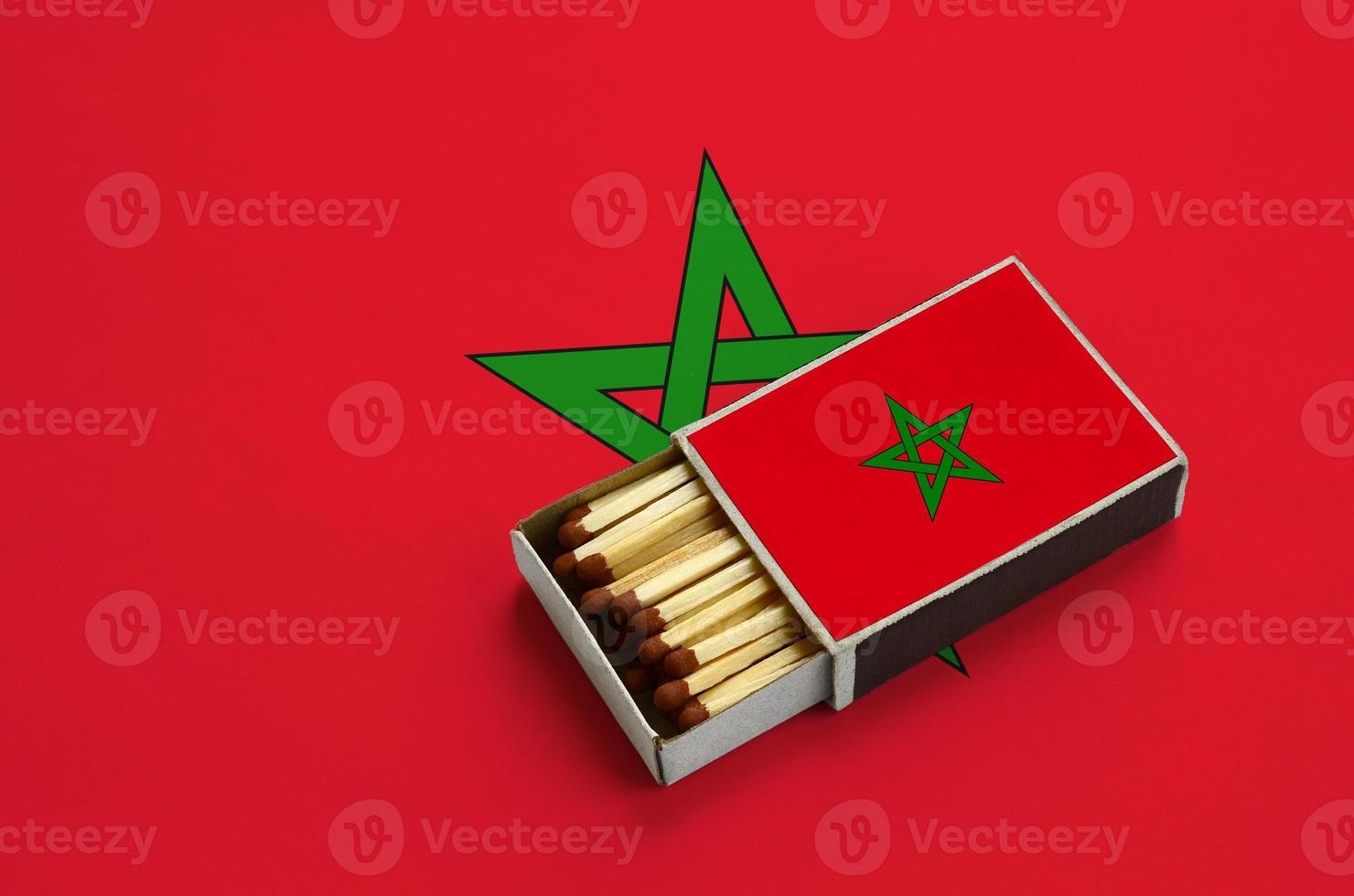 le drapeau du maroc est affiché dans une boîte d'allumettes ouverte, qui est remplie d'allumettes et repose sur un grand drapeau photo