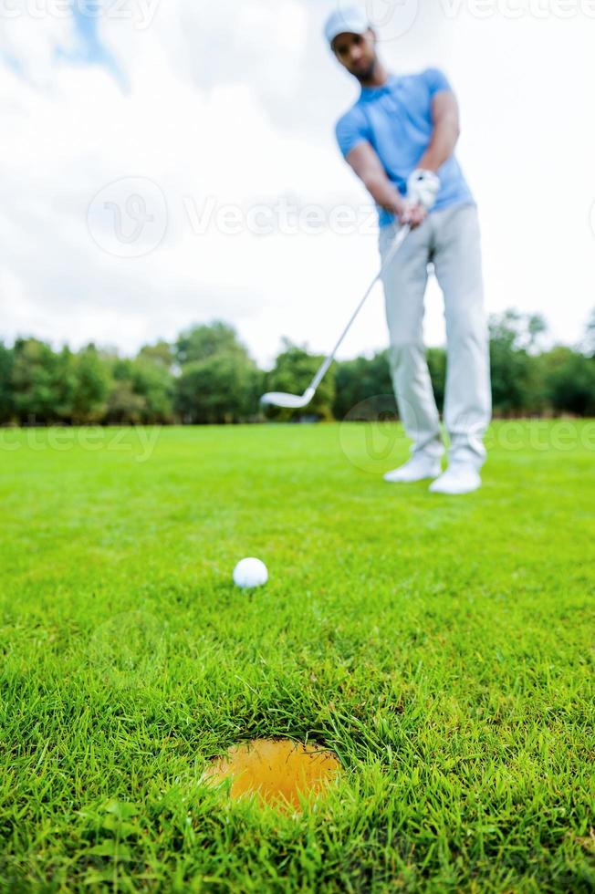 coup de golfeur. toute la longueur du jeune homme en vêtements de sport  jouant au golf en se tenant debout sur le vert avec un trou au premier plan  13287369 Photo de