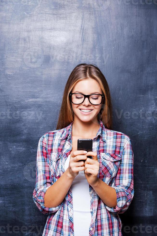 berceau téléphonique. jeunes femmes gaies tenant le téléphone et souriant debout contre le tableau noir photo