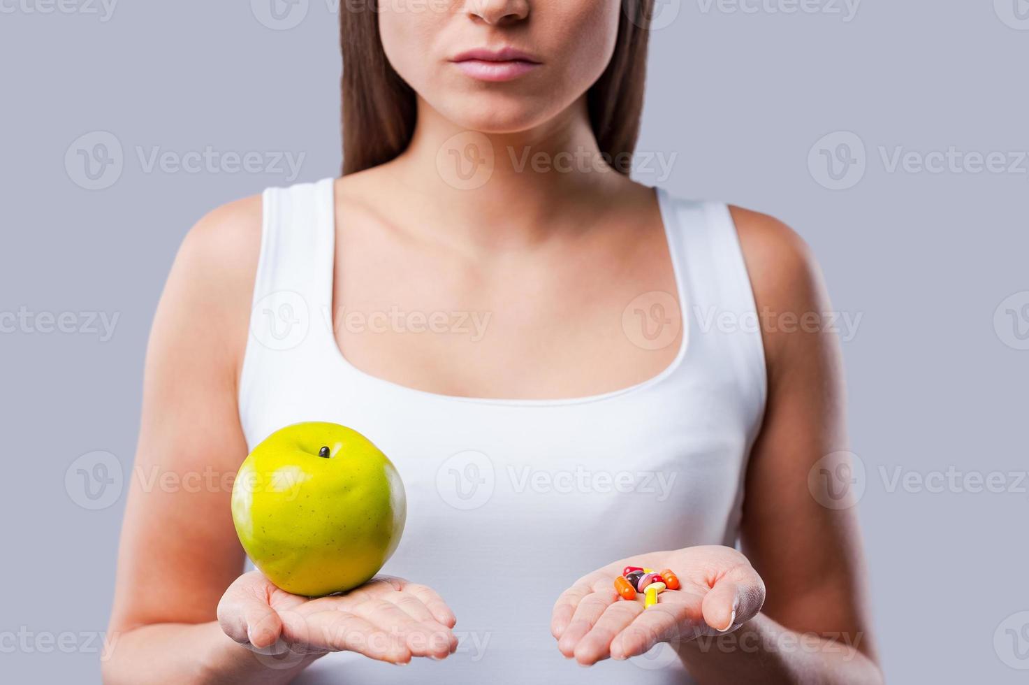 faites votre choix photo recadrée d'une jeune femme tenant une pomme et des pilules dans ses mains