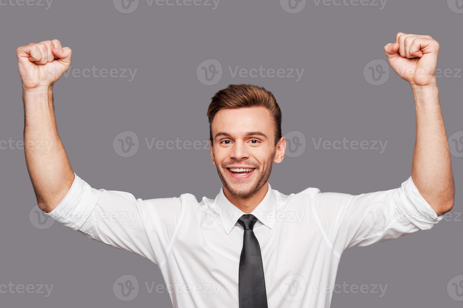 c'est le succès heureux jeune homme en tenues de soirée gesticulant et souriant en se tenant debout sur fond gris photo