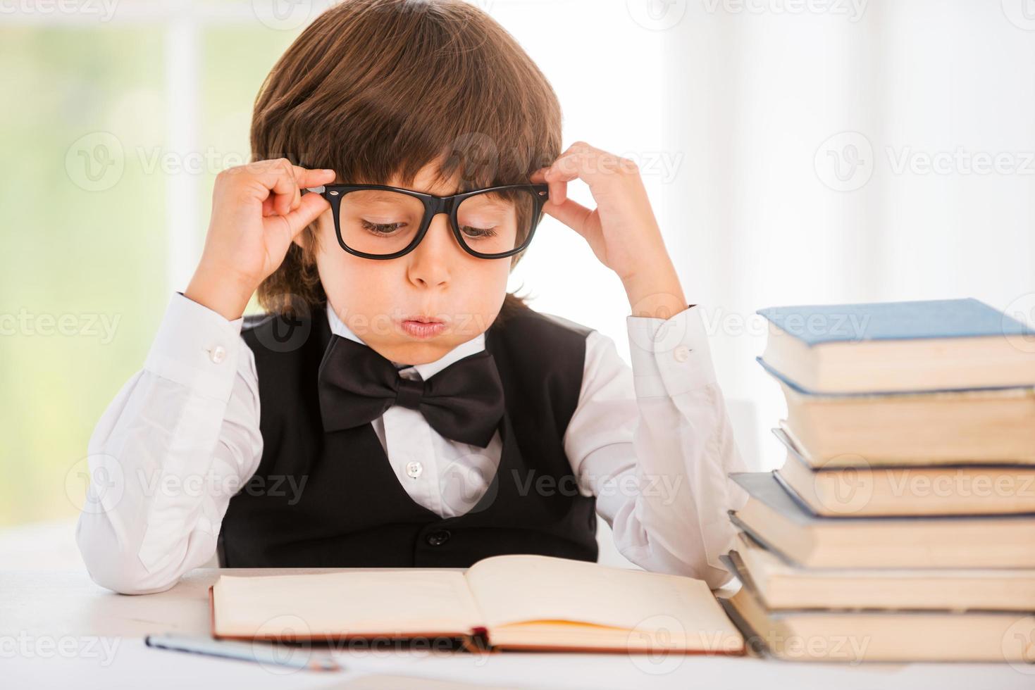 fatigué d'étudier. petit garçon fatigué regardant le livre et tenant ses lunettes assis à la table photo