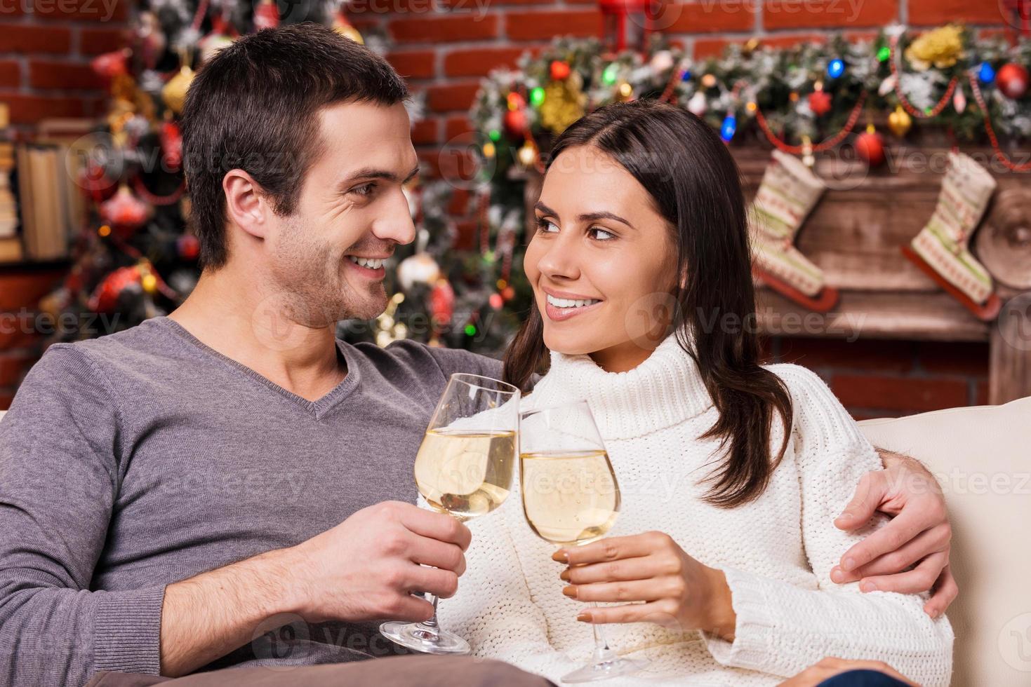 bonne année beau jeune couple d'amoureux se liant les uns aux autres et tenant des verres à vin avec l'arbre de noël en arrière-plan photo