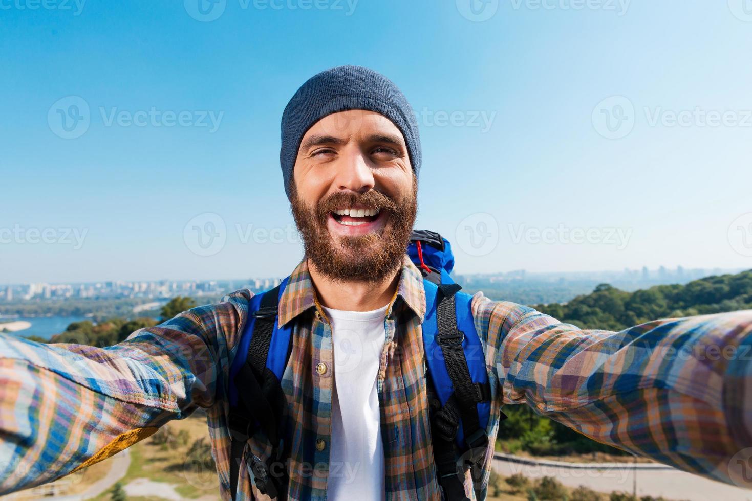 je suis dans le plus bel endroit beau jeune homme portant un sac à dos et prenant une photo de lui-même