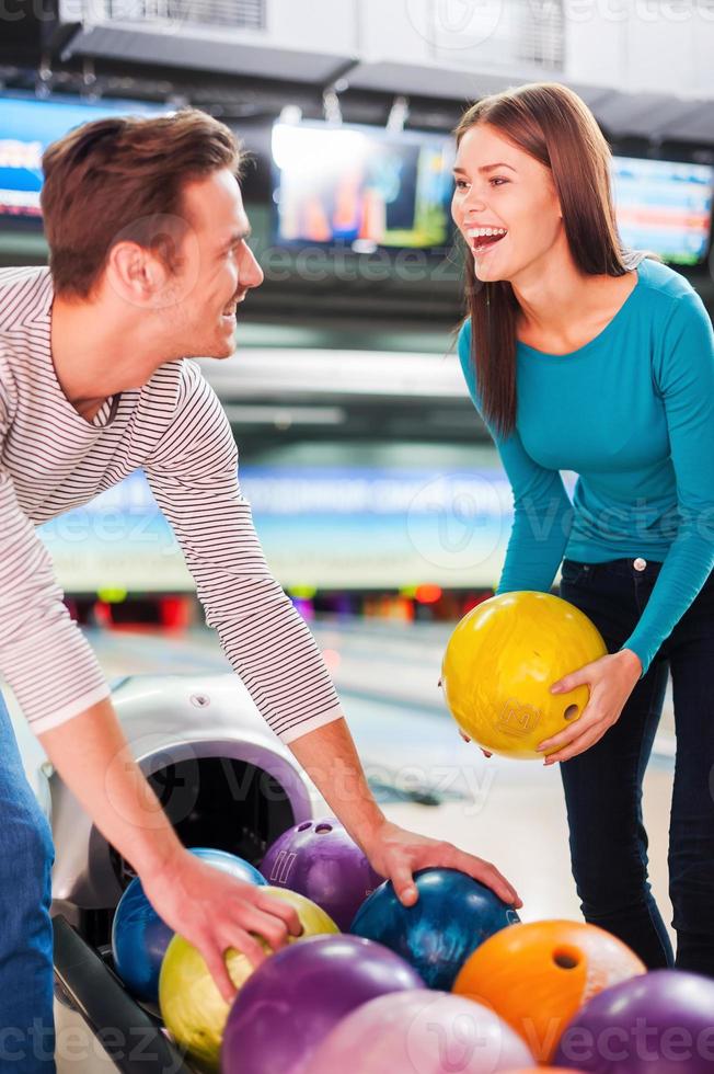 amis joyeux. joyeux jeune couple se regardant et choisissant des boules de bowling tout en se tenant contre les pistes de bowling photo