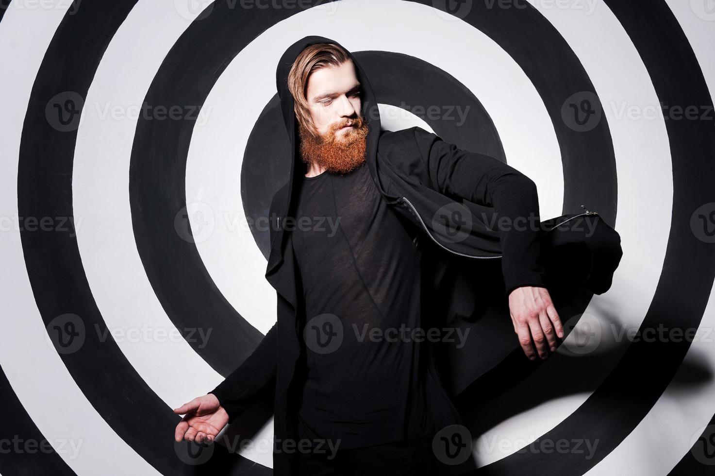 confiant dans son look parfait. beau jeune homme barbu ajustant son sweat-shirt et regardant par-dessus l'épaule en se tenant debout sur le fond de la cible photo