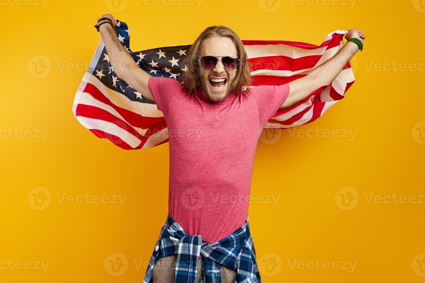 excité jeune homme portant un drapeau américain en se tenant debout sur fond jaune photo