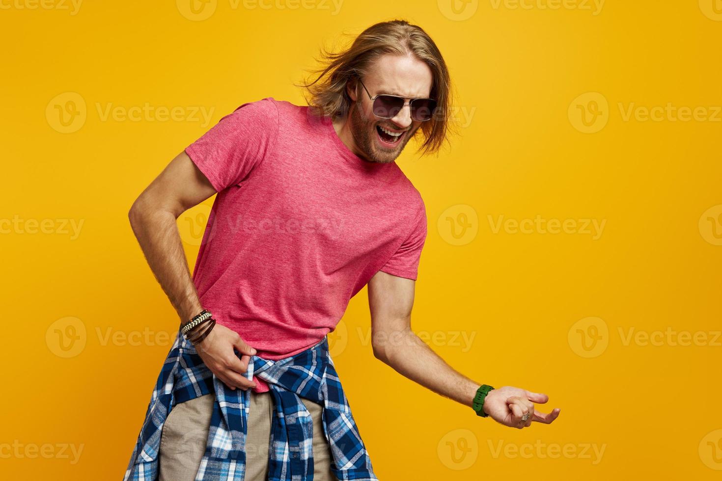 beau jeune homme gesticulant guitare et souriant en se tenant debout sur fond jaune photo