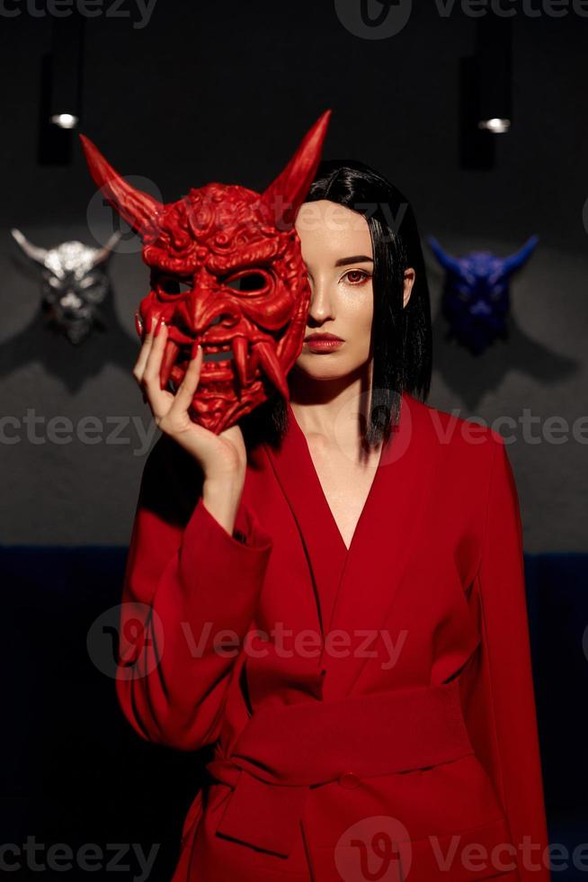 anime femme en costume rouge avec coupe de cheveux courte, cheveux noirs. une fille tueuse dans une veste rouge avec un masque japonais rouge. portrait beauté photo