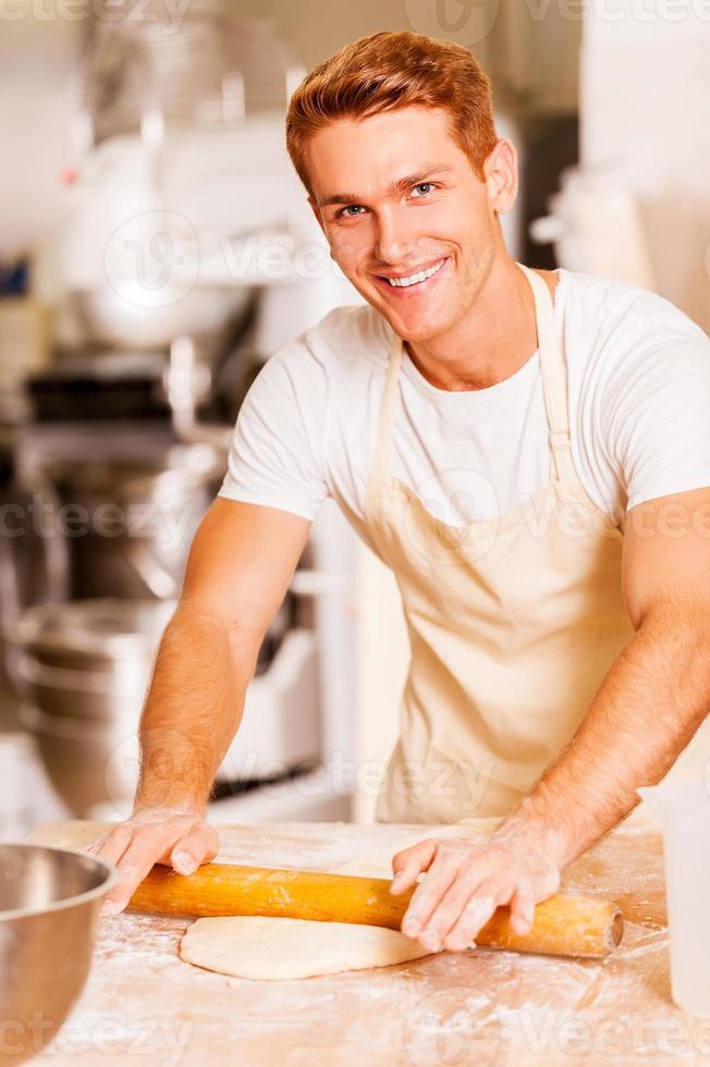 homme roulant la pâte. beau jeune boulanger souriant étalant la pâte avec un rouleau à pâtisserie photo