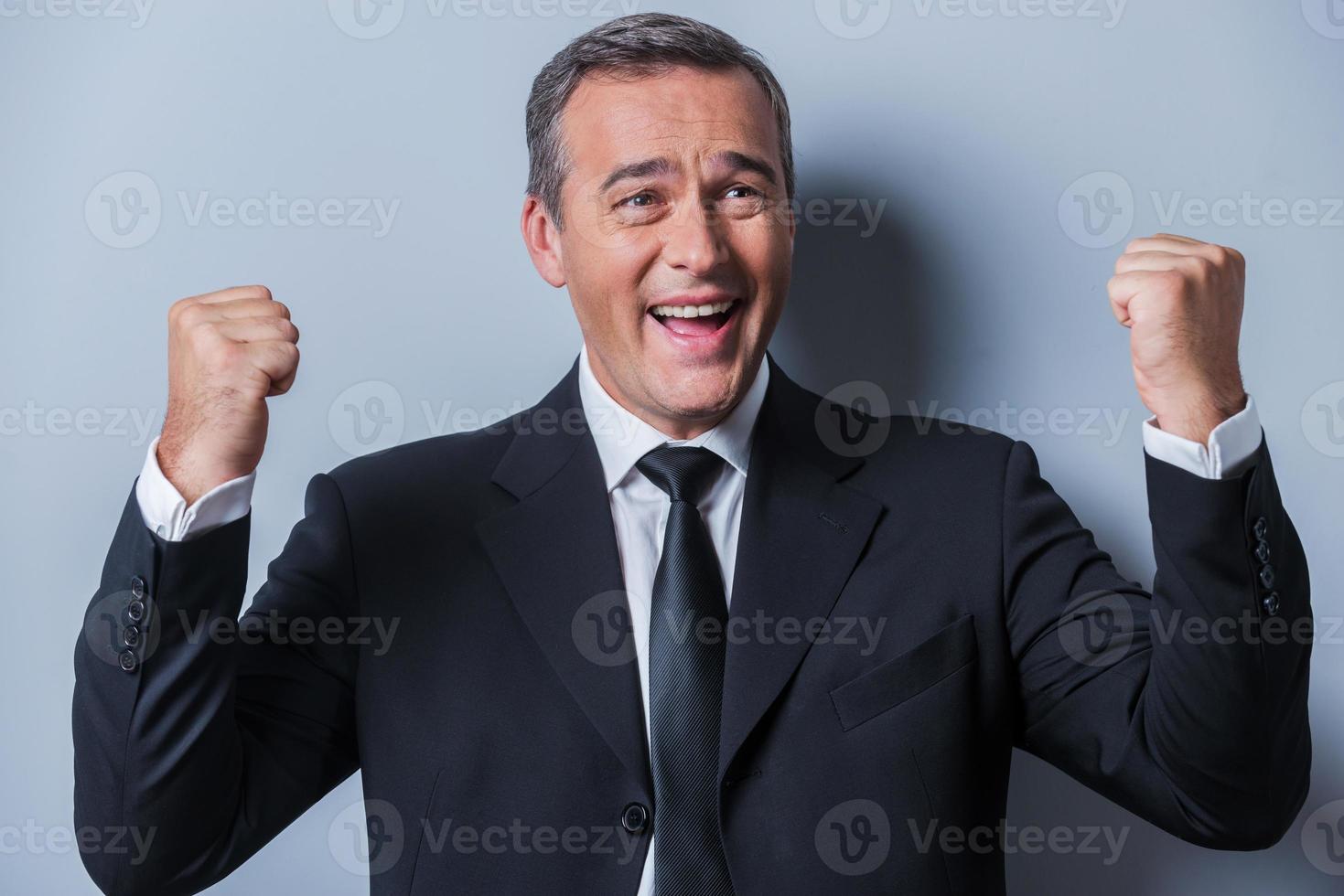 Un homme d'affaires qui réussit. heureux homme mûr en tenues de soirée gesticulant et souriant en se tenant debout sur fond gris photo