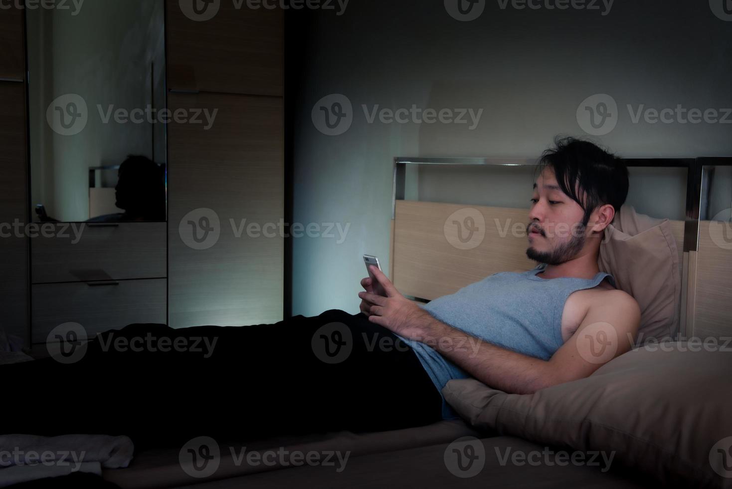 jeune homme utilisant un téléphone portable sur le lit la nuit. photo