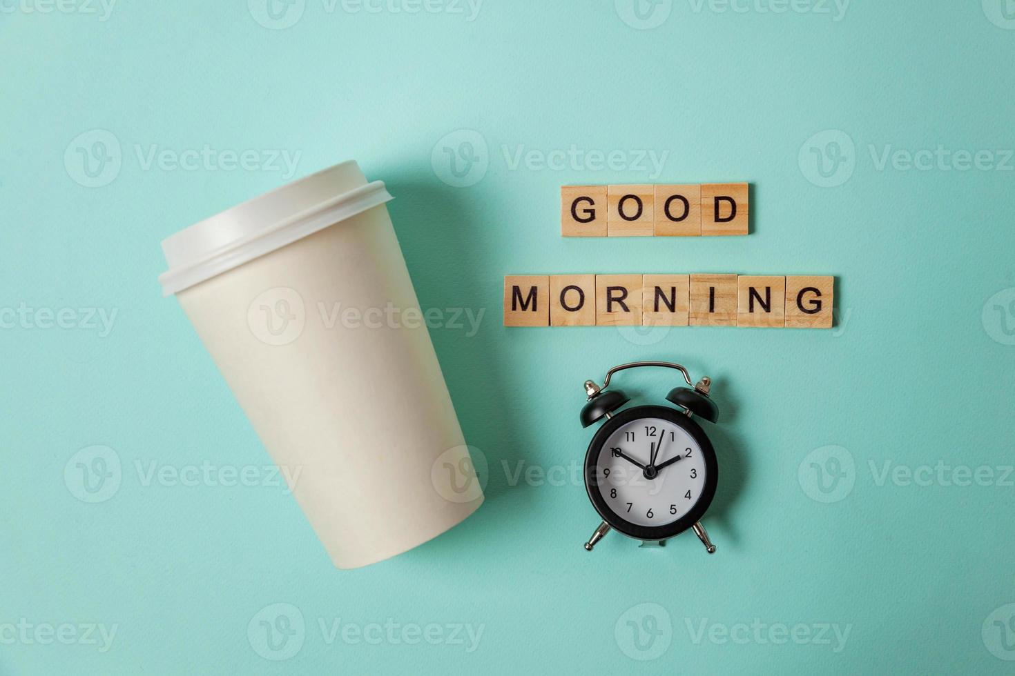 tasse à café en papier design simplement plat et réveil sur fond bleu pastel coloré à la mode. boisson à emporter et boisson du petit déjeuner. bonjour réveillez-vous concept éveillé. espace de copie vue de dessus. photo