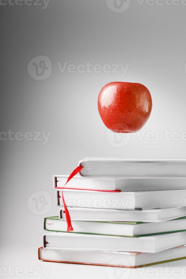 une pomme rouge plane au-dessus d'une pile de livres sur un fond clair. photo