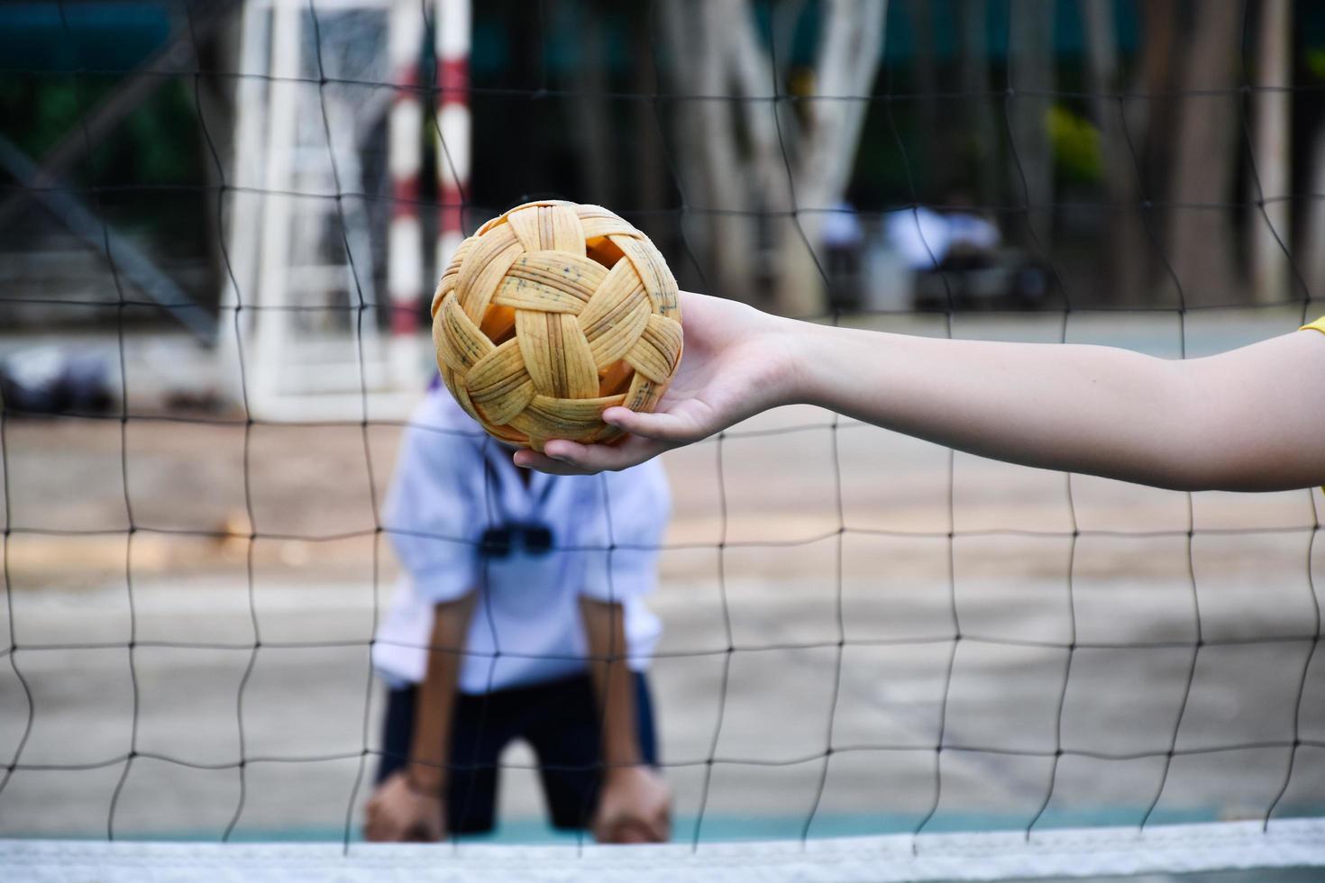 sepak takraw ball, sport traditionnel des pays d'asie du sud-est, tenant dans la main une jeune joueuse sepak takraw asiatique devant le filet avant de la lancer à un autre joueur pour qu'il passe par-dessus le filet. photo