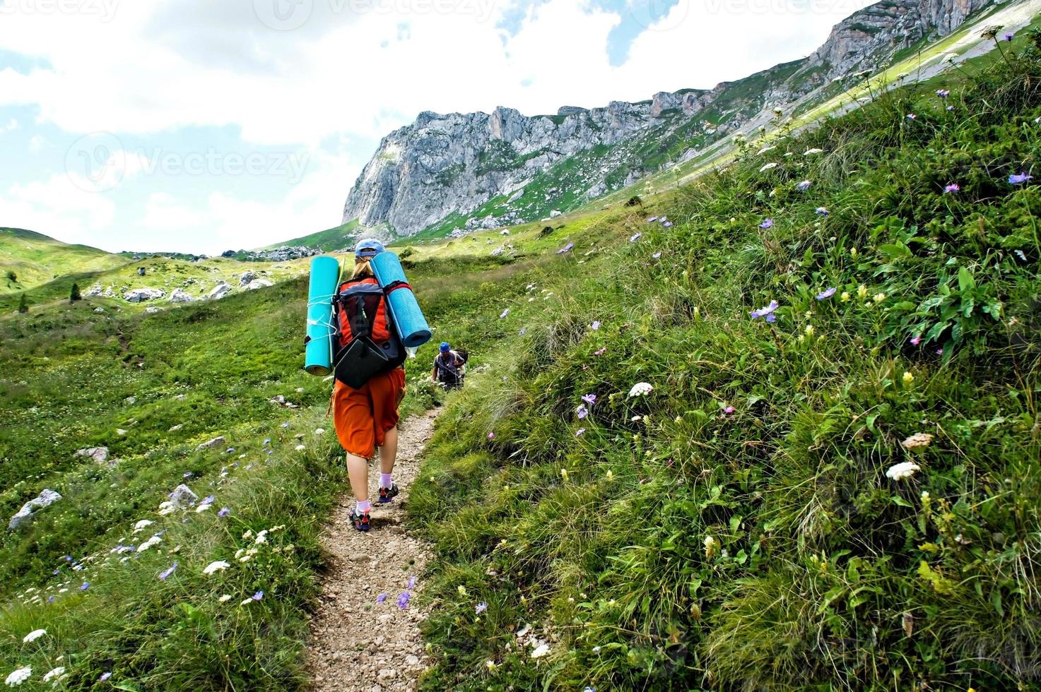 jeune femme caucasienne randonneur par derrière avec sac à dos marchant sur un sentier de montagne sur fond de végétation verte en été dans les montagnes du caucase photo